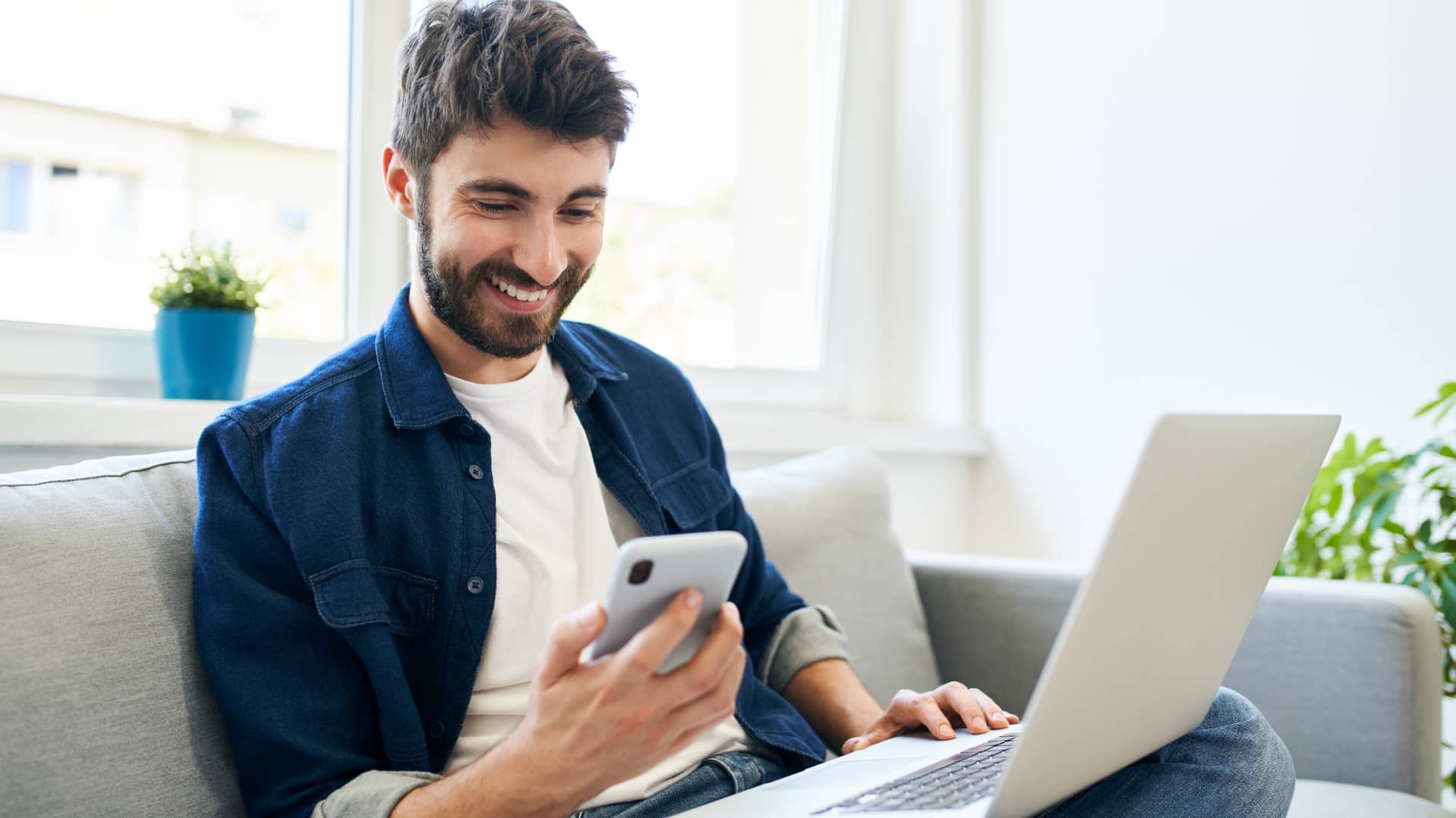 chico joven en el sofa de casa a punto de hacer la recarga de su celular con hermobile chico joven en el sofa de casa a punto de hacer la recarga de su celular con hermobile